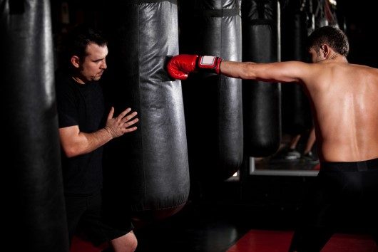 Boxer training with his coach Young Boxer training with his coach on a punching bag at a gym