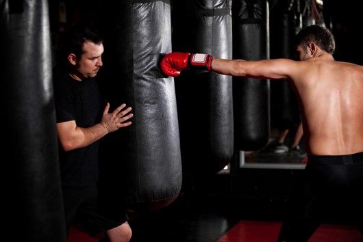 Young Boxer training with his coach on a punching bag at a gym